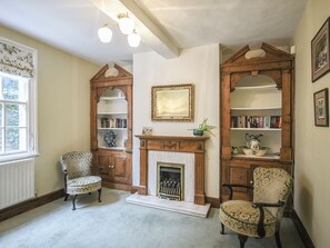 A traditional room with a fireplace, bookshelves, and two patterned chairs.