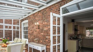 A conservatory with a brick wall, white furniture, and a dining area with a table set for two. - 6 bedroom accommodation in Dorrington, near Church Stretton (Dorrington, near Church Stretton)