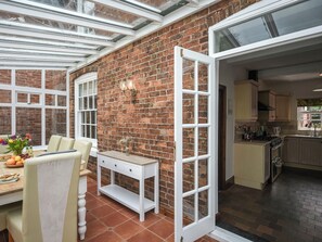 A conservatory with a brick wall, white furniture, and a dining area with a table set for two.