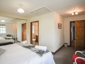 A bedroom with a bed, a mirror, a wooden door, and a bathroom visible through an open door.