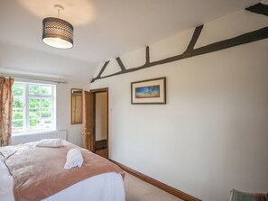 Une chambre à coucher avec un lit, une fenêtre, une porte, un tableau et une poutre en bois au mur.