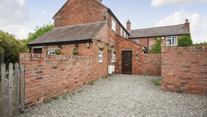 A traditional brick house with a gravel driveway, a wooden gate, and hanging flower baskets. - 6 bedroom accommodation in Dorrington, near Church Stretton (Dorrington, near Church Stretton)