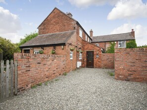 A traditional brick house with a gravel driveway, a wooden gate, and hanging flower baskets.
