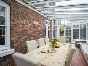 A dining area with a brick wall, white-framed windows, and a wooden table set for four.