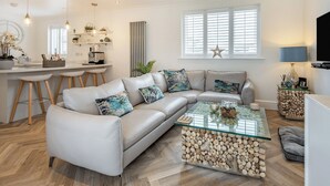 A modern living room with a sofa, a glass coffee table, and a kitchen area in the background. - 3 bedroom accommodation in Rhyl and Prestatyn (Rhyl and Prestatyn)