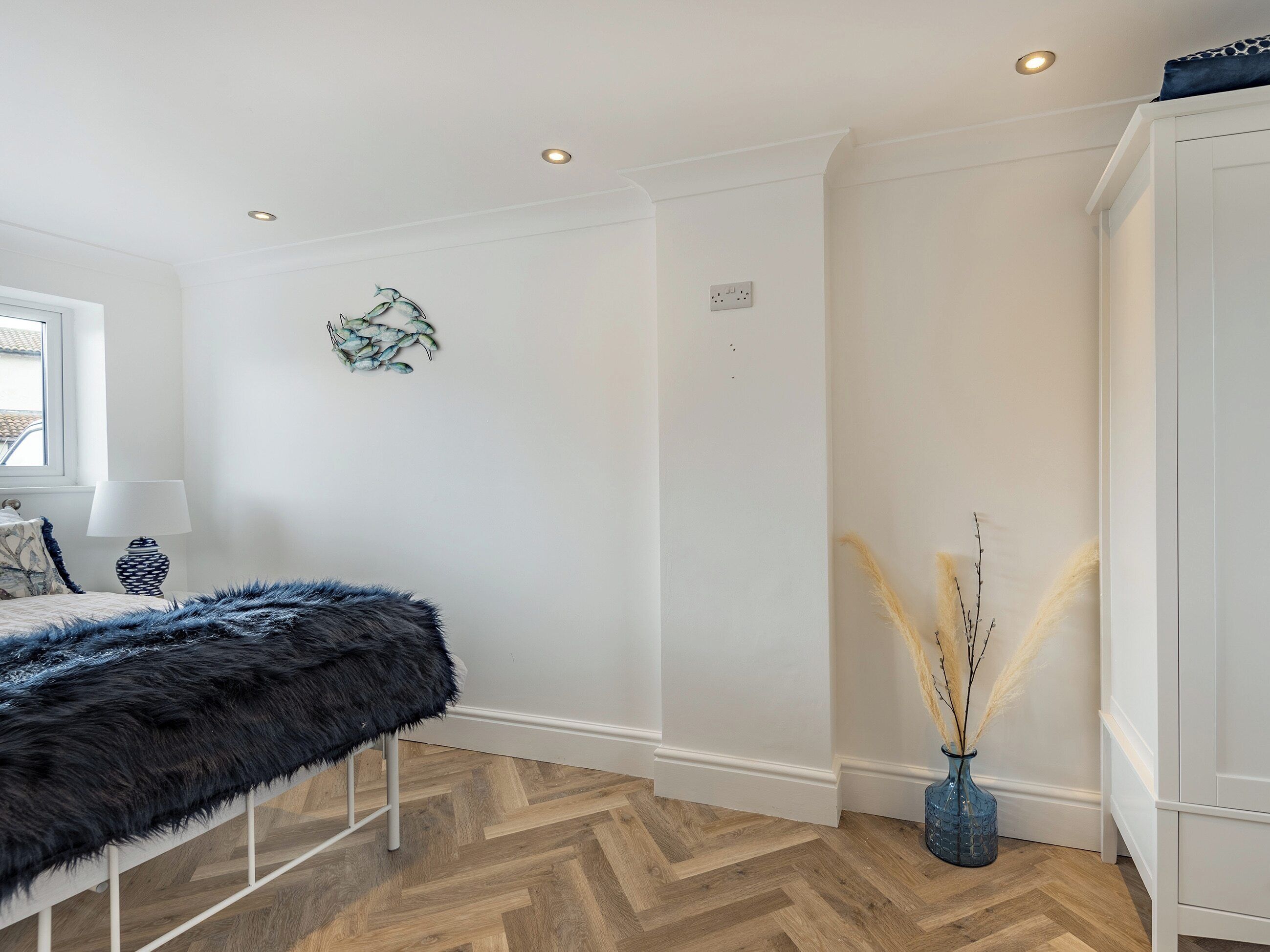 A modern bedroom with a bed, a fluffy bench, a vase with pampas grass, and a white wardrobe.