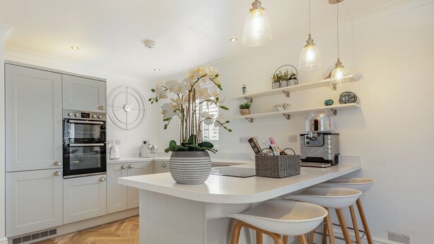 A modern kitchen with white cabinetry, a built-in oven, a coffee machine, and a large island with bar stools. - 3 bedroom accommodation in Rhyl and Prestatyn (Rhyl and Prestatyn)