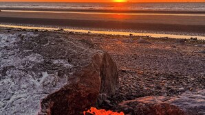 A rocky beach with a fire pit in the foreground and a sunset in the background. - 3 bedroom accommodation in Rhyl and Prestatyn (Rhyl and Prestatyn)