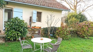 A house with a tiled roof, a small garden with a round table and wicker chairs, and a blue door. - Studio Confort Cerise (Bayonne)