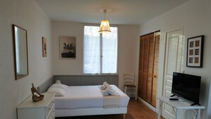 A bedroom with a bed, bedside table, TV, wardrobe, and a window with blinds. - Studio Confort Cerise (Bayonne)
