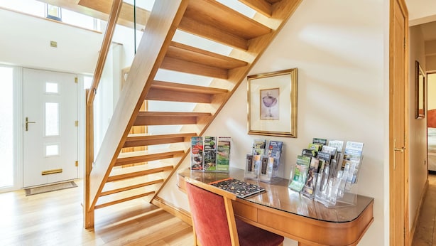 A wooden staircase, a desk with magazines, and a framed picture on the wall.