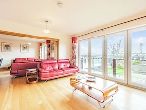 A spacious living room with a red leather sofa, a wooden coffee table, and large windows offering a view of the city. - 6 bedroom accommodation in Cinderford (Cinderford)