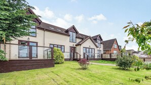 A modern two-story house with a well-maintained lawn, a wooden deck, and a large window overlooking the garden.