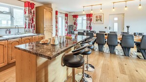 A modern kitchen with wooden cabinets, a marble countertop, and a dining area with a wooden table and chairs.
