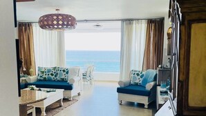 A spacious living room with a view of the ocean, featuring two sofas, a dining table, and a large wooden cabinet.