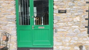A green door with a window, a stone wall, and a sign that reads "ONE". - 1 Greenswood Court (Brixham)