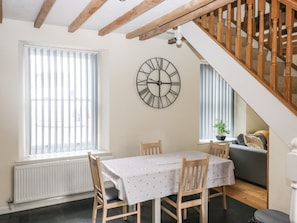 A dining area with a table and chairs, a wall clock, a staircase, and a window with blinds.