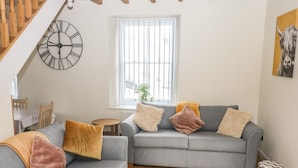 A living room with a grey sofa, a wooden floor, a round table, and a large wall clock. - 1 Greenswood Court (Brixham)
