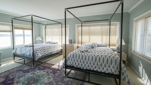 A bedroom with two four-poster beds, a large rug, and a view of the outdoors.