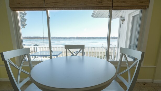A round table with four white chairs in a room with large windows overlooking a body of water.
