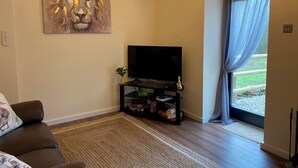A living room with a sofa, a flat-screen TV, a bookshelf, and a painting on the wall. - 1 bedroom accommodation in Stockton Brook, near Leek (Stockton Brook, near Leek)