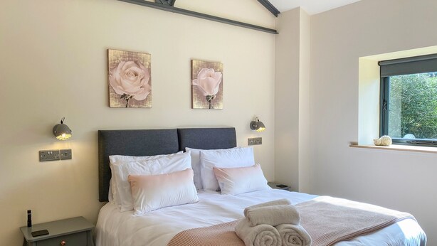 A neatly made bed with white linens and a pink blanket, two wall-mounted light fixtures, and two framed floral paintings above the bed. - 1 bedroom accommodation in Stockton Brook, near Leek (Stockton Brook, near Leek)