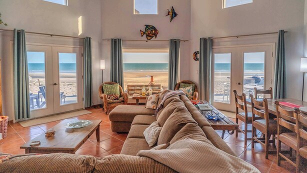 Ein großzügiger Wohnbereich mit einer großen Couch, Esstisch und Stühlen mit Blick auf einen Strand.