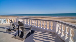 Ein Balkon am Strand mit Blick auf das Meer, ausgestattet mit zwei Adirondack-Stühlen und einem weißen Geländer.