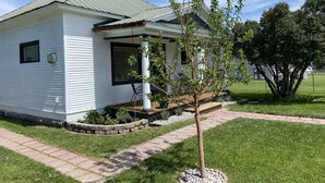 Ein weißes Einfamilienhaus mit grünem Dach, einer Veranda mit Schaukel und einem kleinen Baum im Vorgarten.
