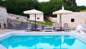 A swimming pool with lounge chairs and umbrellas, surrounded by stone walls and greenery. - DONNAPAOLA MODERN FARM (Altamura)