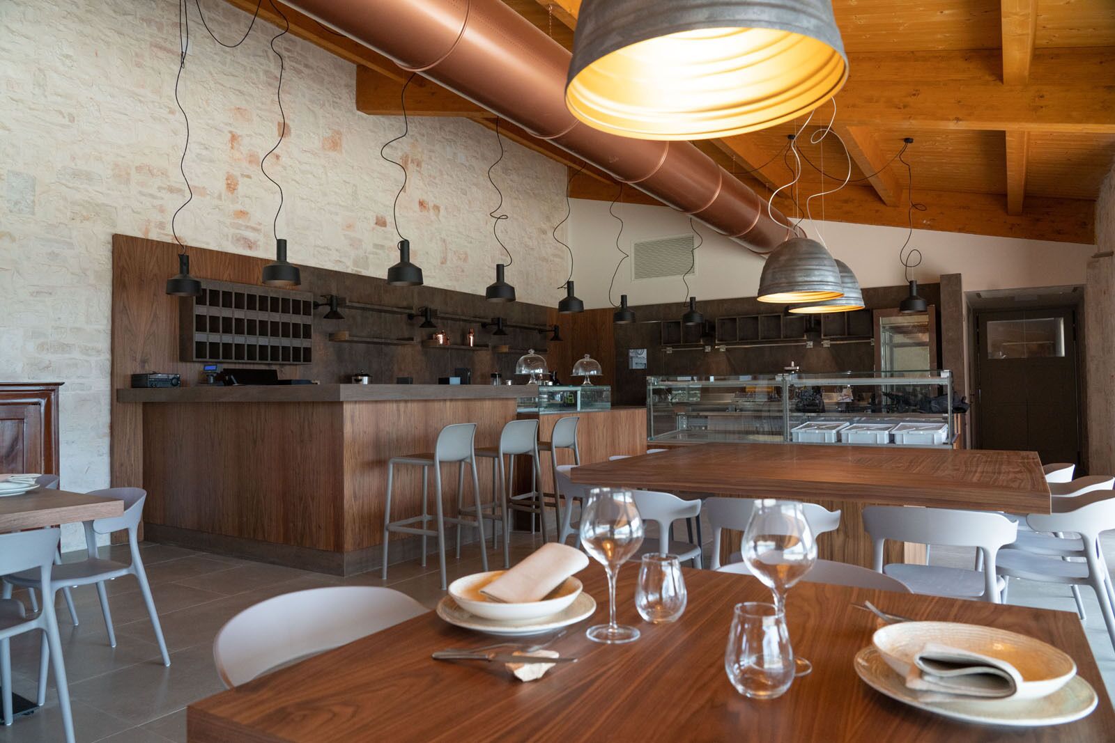 Un restaurant moderne doté d’un bar en bois, de hauts plafonds, de conduits apparents et d’un mobilier combinant des éléments en métal et en bois.