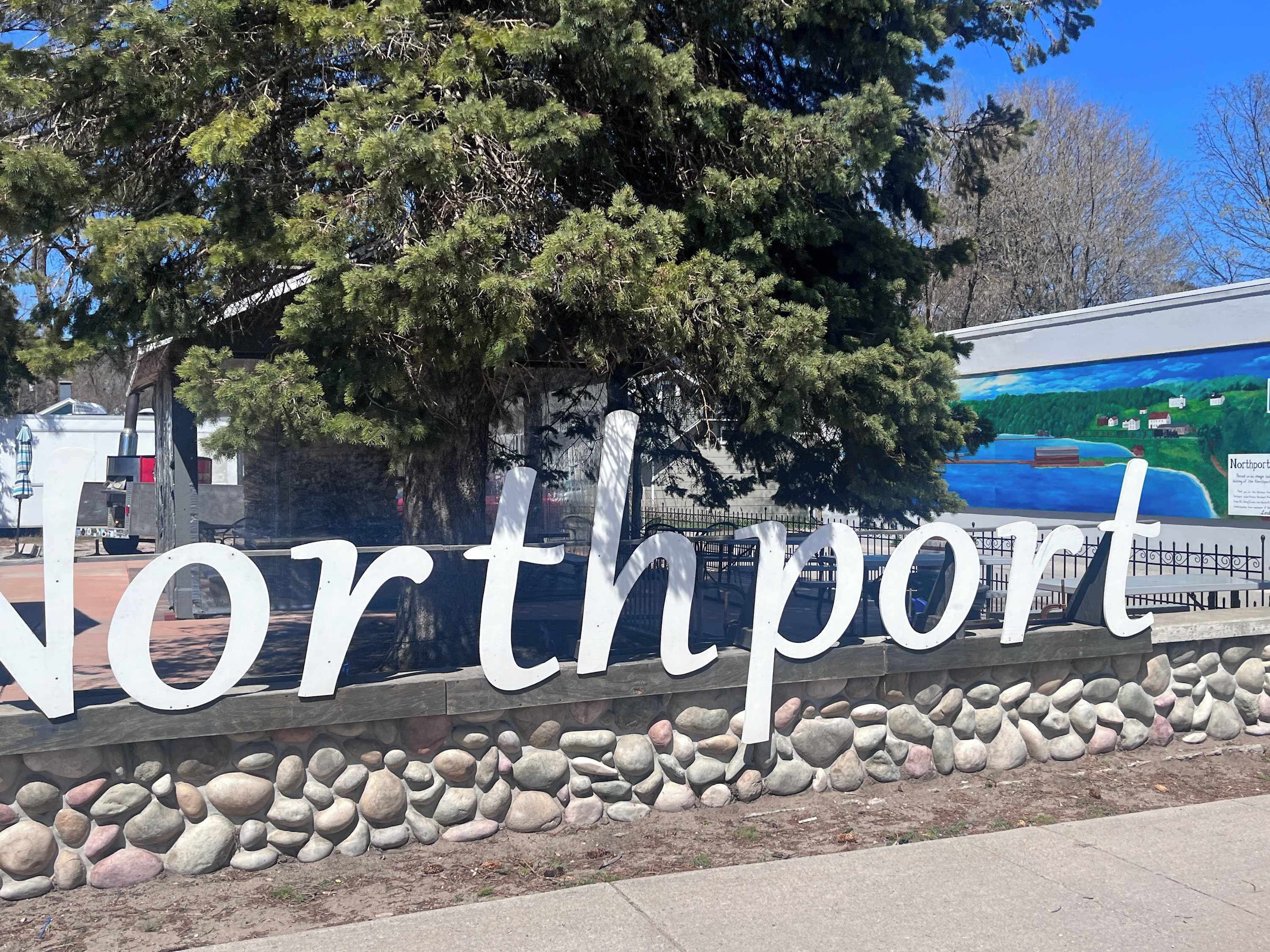 A large sign with the name "Northport" in white letters on a stone wall, with a mural in the background depicting a landscape.