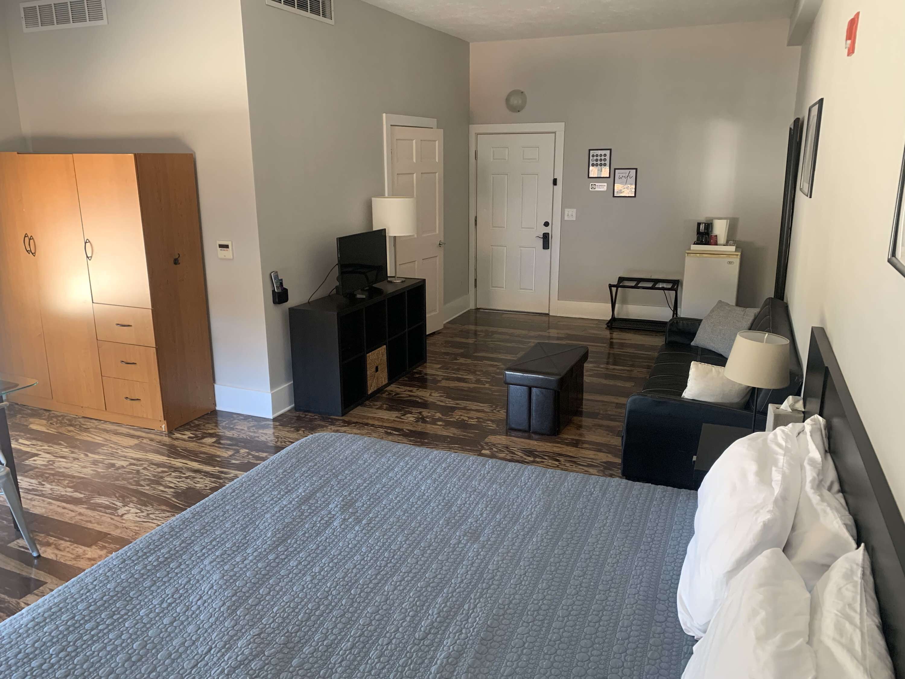 A hotel room with a bed, a desk, a chair, a small table, a TV, and a wardrobe.