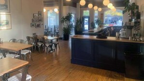 A restaurant interior with wooden tables and chairs, a central bar area, and potted plants. - Northport Inn Boutique Hotel Room 4 (Northport)