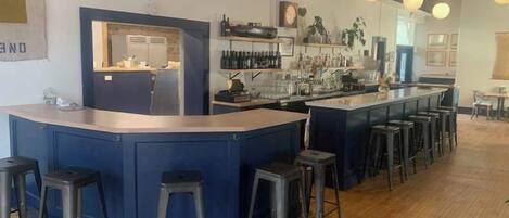 Zona de bar con taburetes, mostrador y estantes con botellas.