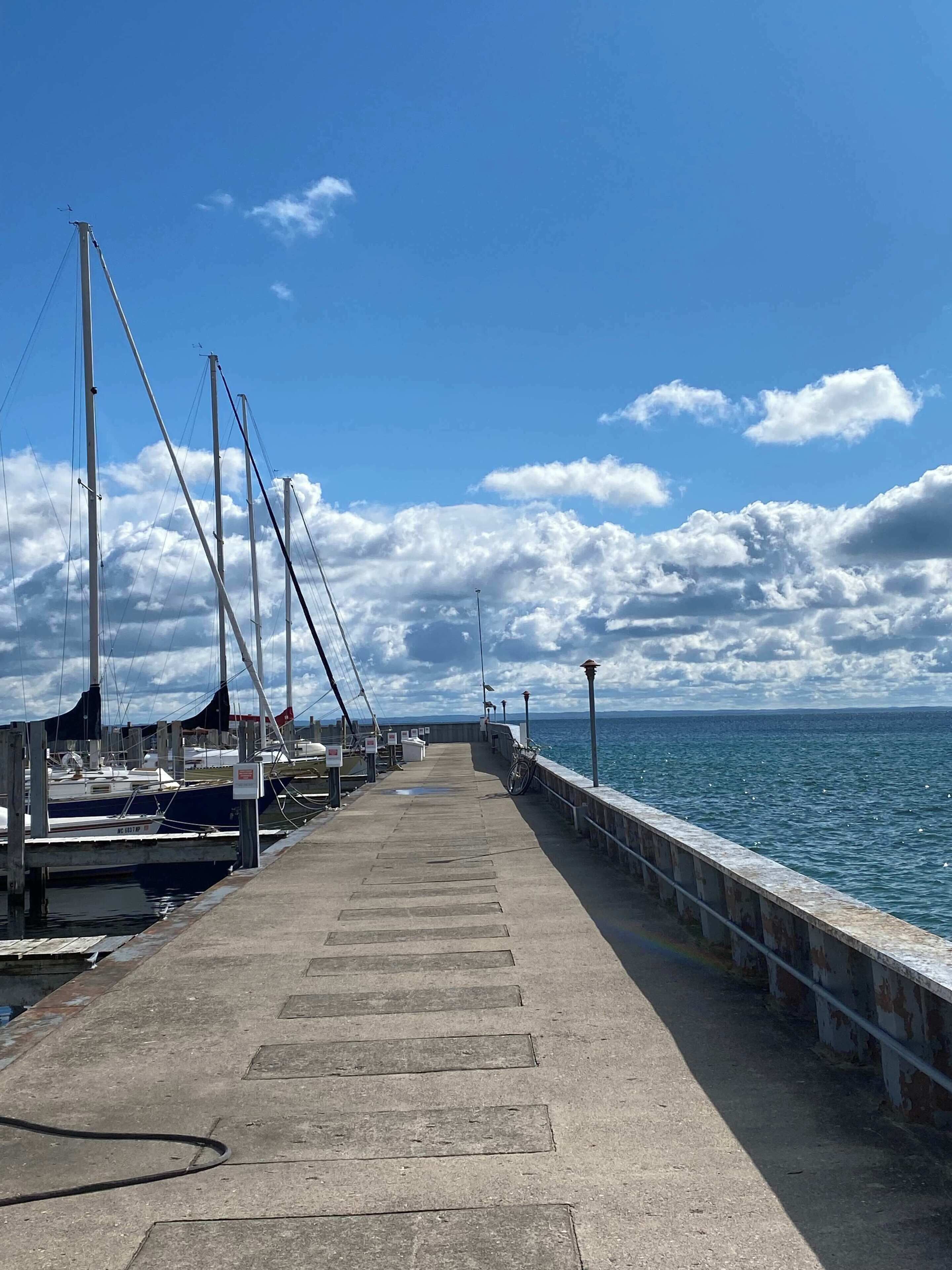A pier extending into the sea with boats docked on the left, a clear sky, and a calm sea.