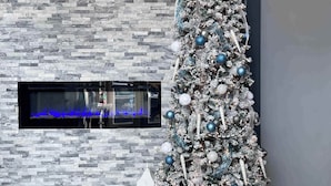 A modern living room with a tall, decorated Christmas tree, a fireplace, and contemporary lighting fixtures.