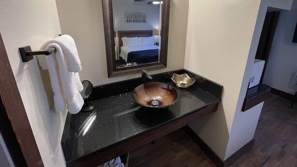A bathroom with a black countertop, a copper sink, a mirror above the sink, and a towel rack with a white towel. - Welcome To The New Kanab Lodge Suite 22 (Kanab)