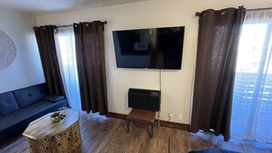 A living room with a flat-screen TV mounted on the wall, a dark-colored sofa, a wooden coffee table, and a bench. - Welcome To The New Kanab Lodge Suite 22 (Kanab)
