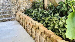 Una escala de pedra que mena a una porta de fusta, envoltada per una paret de pedra i vegetació verda abundant.