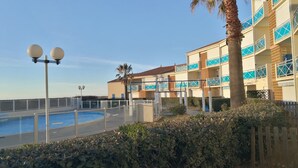A hotel with a swimming pool, palm trees, and a clear blue sky. - Beachfront apartment with pool, air conditioning and wifi (Frontignan)