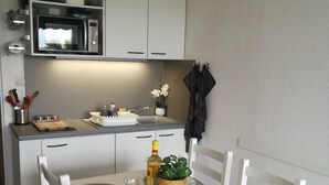 A compact kitchen with white cabinets, a microwave, and a small countertop. There is a dining table set with plates, glasses, and a bottle of olive oil. - Beachfront apartment with pool, air conditioning and wifi (Frontignan)