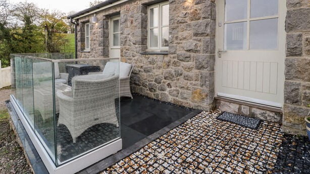 Un bâtiment en pierre doté d’un patio vitré comprenant un canapé en osier et une table en verre.
