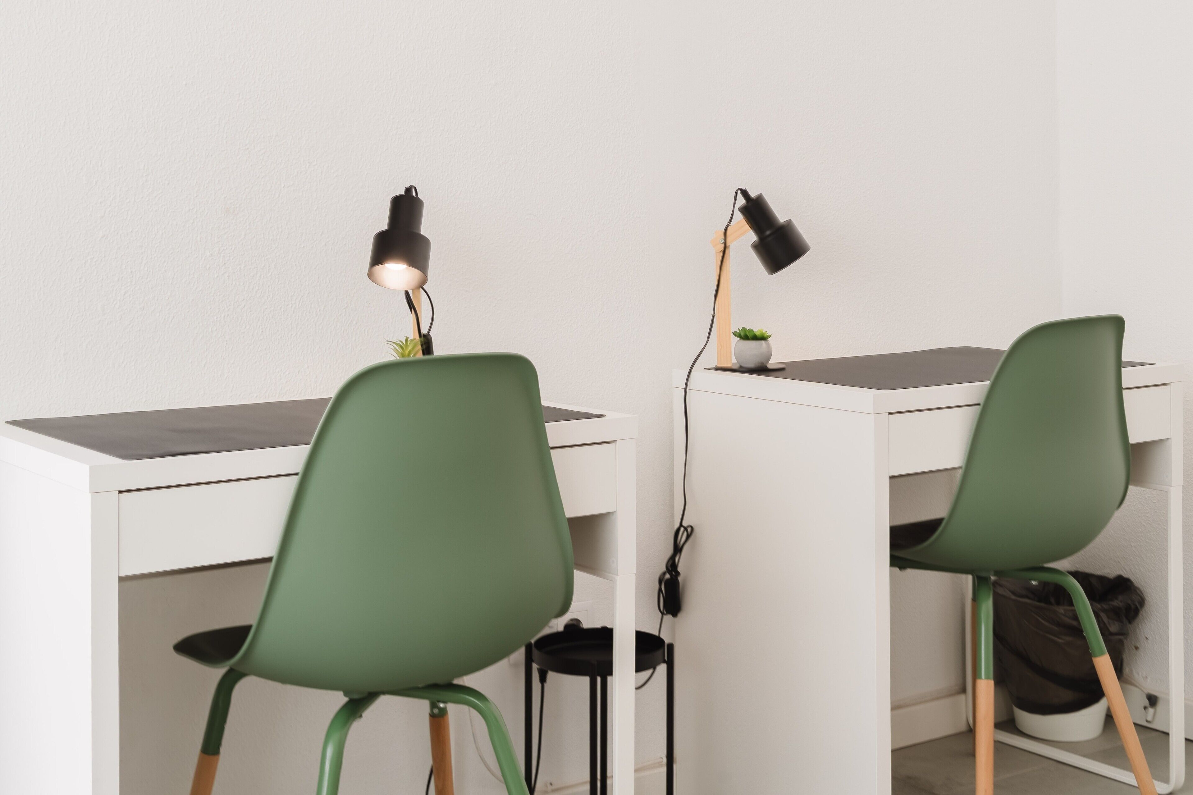 Zwei Schreibtische mit grünen Stühlen, jeweils mit einer Schreibtischlampe.