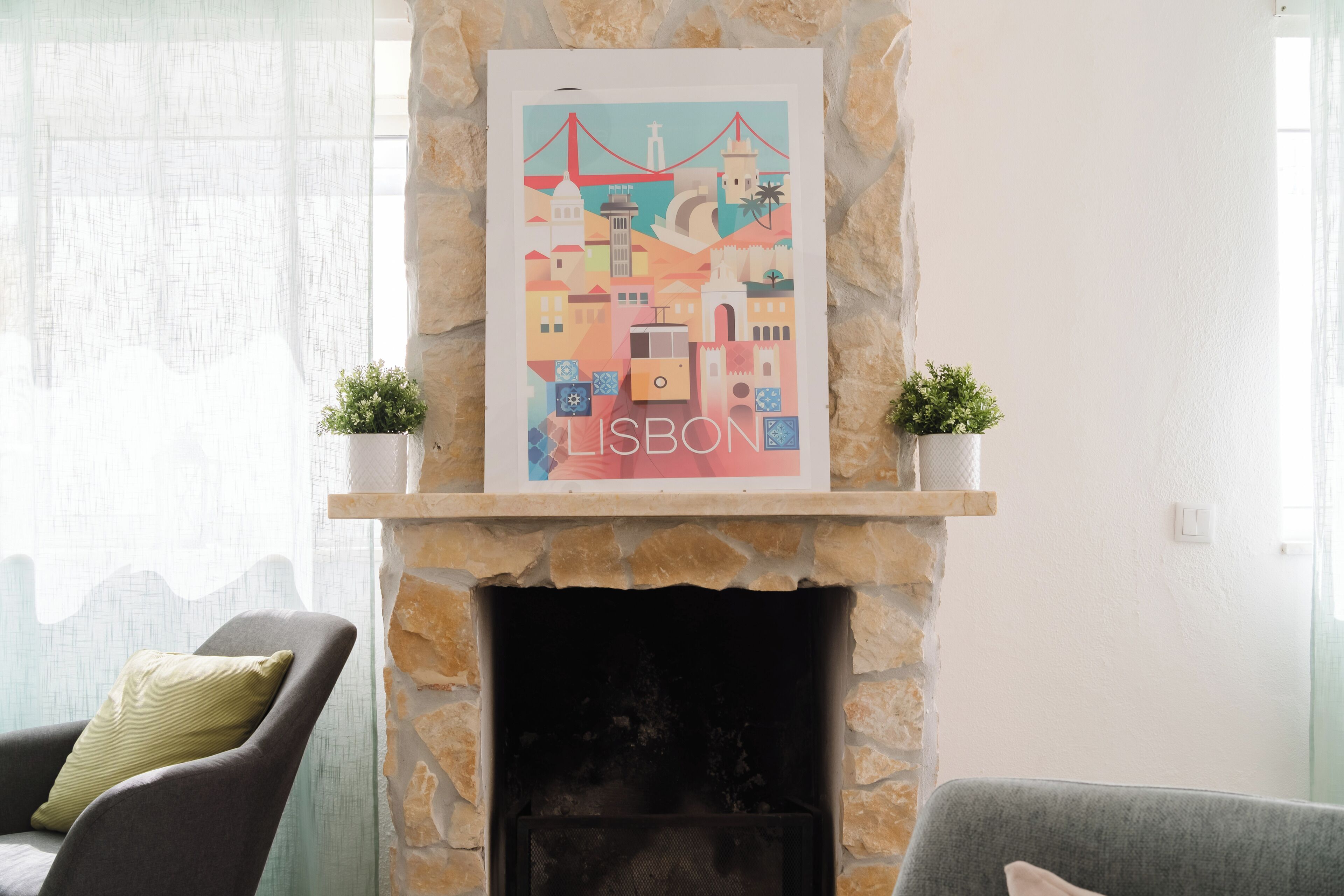 A fireplace with a framed cityscape poster of Lisbon, flanked by two potted plants.