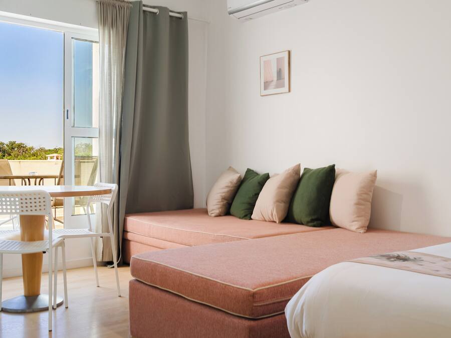 Una habitación de hotel moderna con sofá cama, una pequeña mesa y sillas, y vistas al exterior.