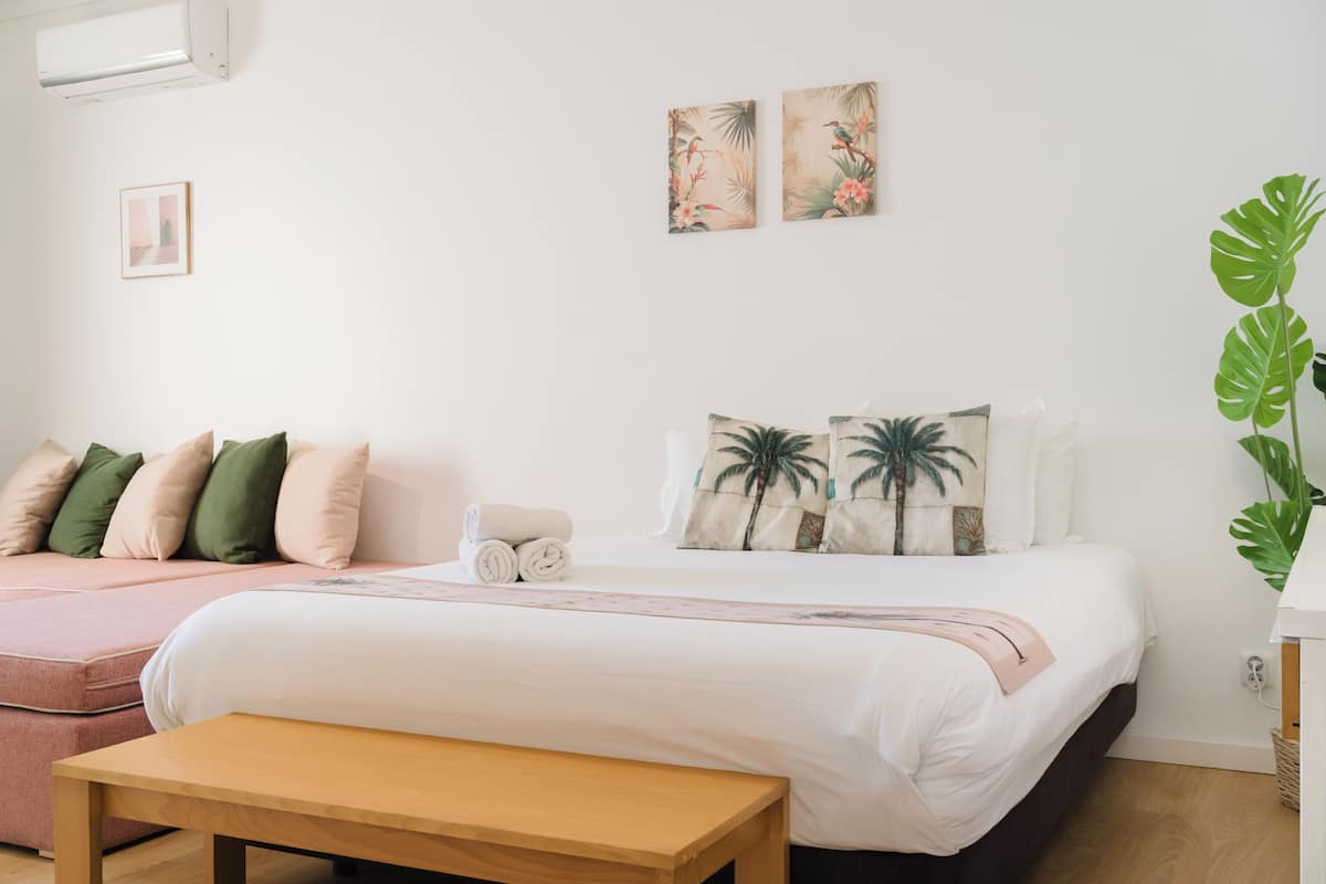A bedroom with a bed, a bench, a potted plant, and artwork on the wall.