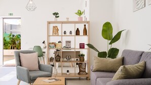 A modern living room with a grey armchair, a grey sofa, and a wooden coffee table. There is a bookshelf with various decorative items and plants. - Villa Paraiso Da Caparica (Almada)