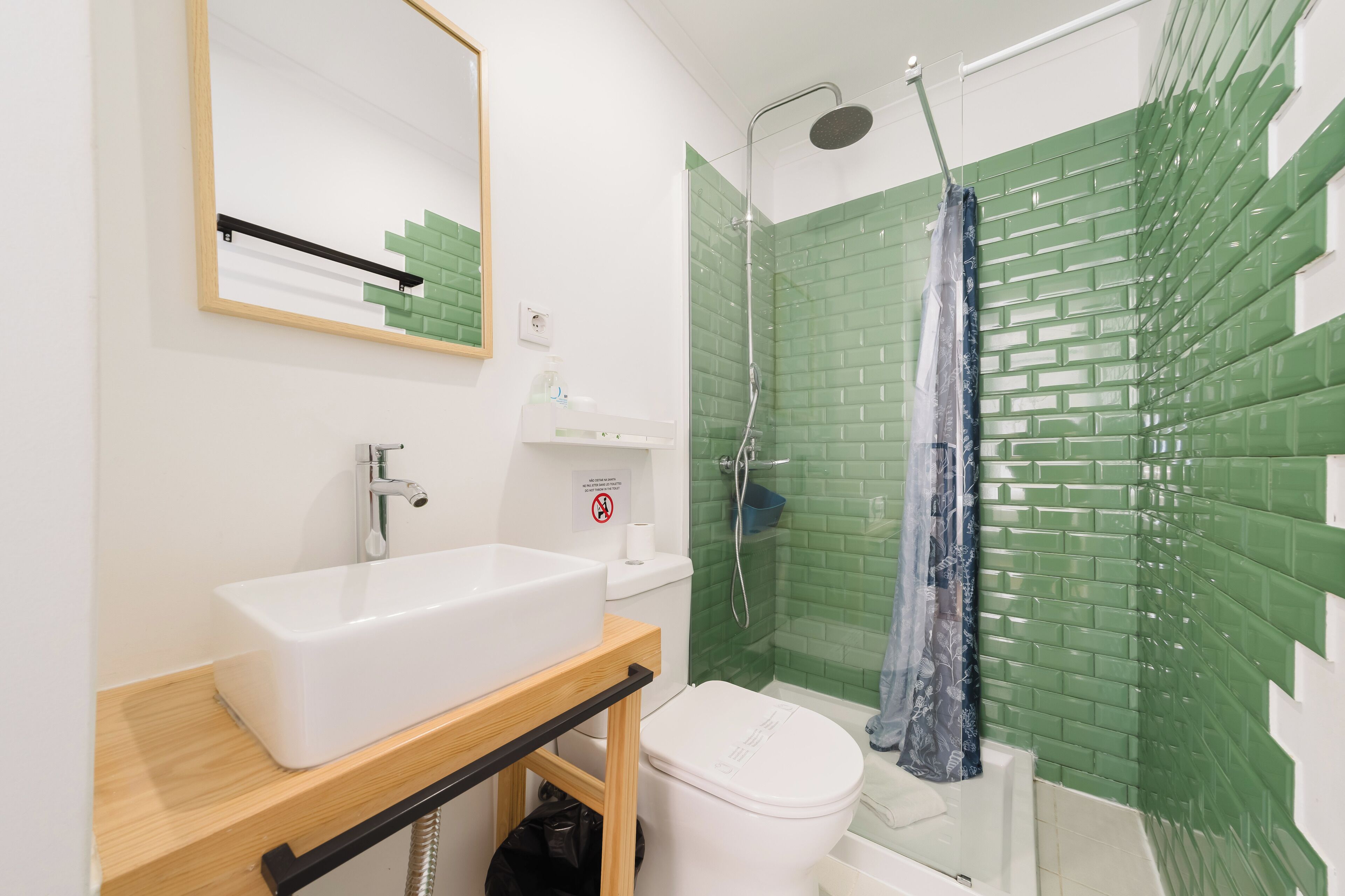 Un bagno con lavandino bianco, un water, una doccia con piastrelle verdi e uno specchio con cornice in legno.
