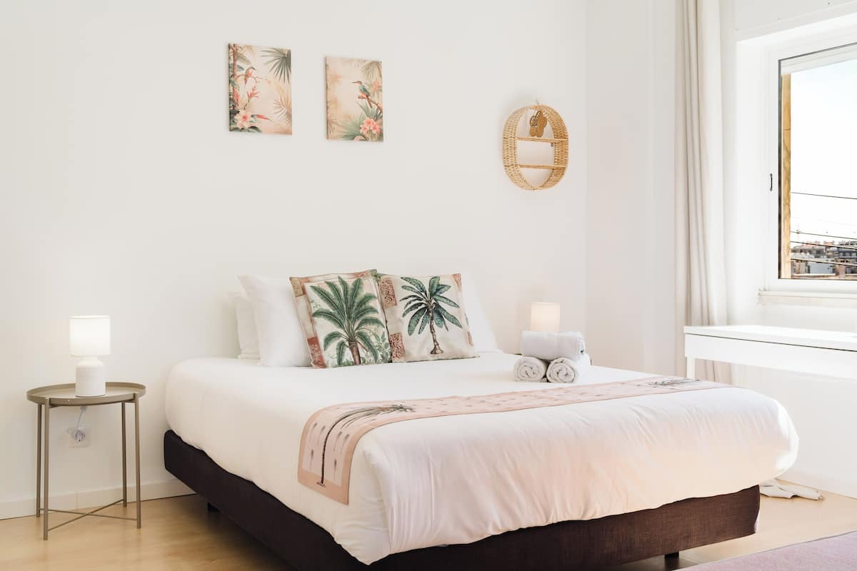 A neatly arranged bedroom with a bed, bedside lamps, and wall art.